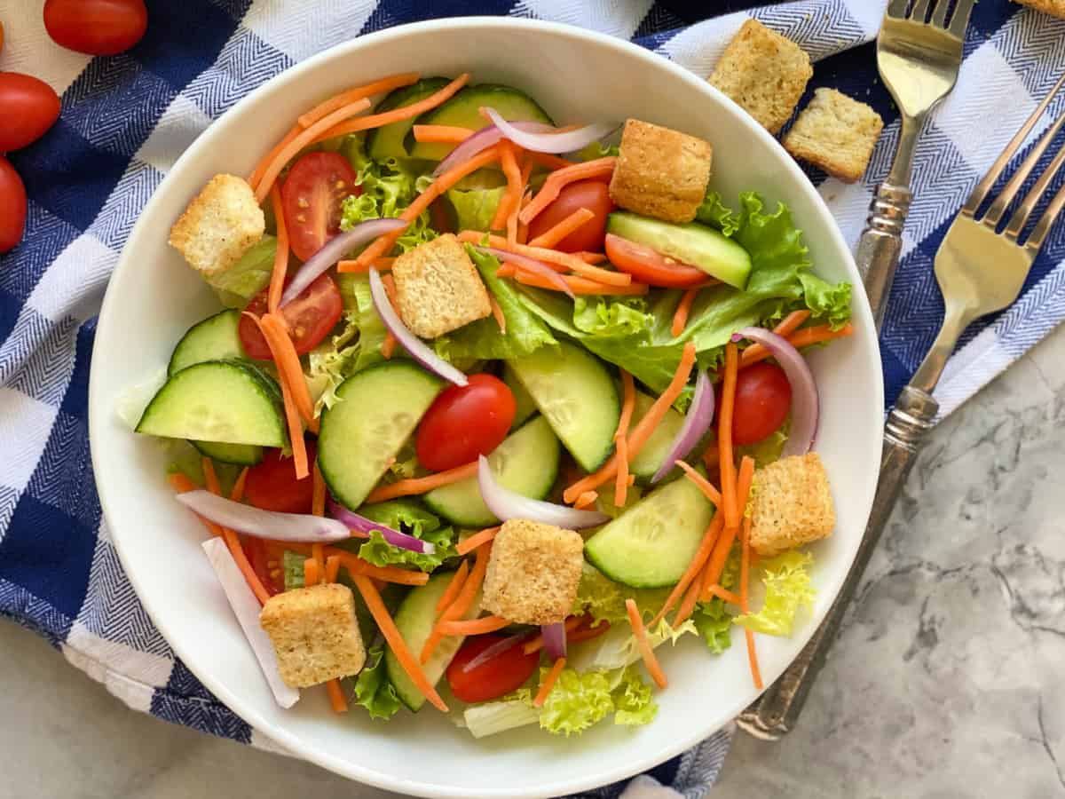 White bowl filled with salad and two forks next to it.