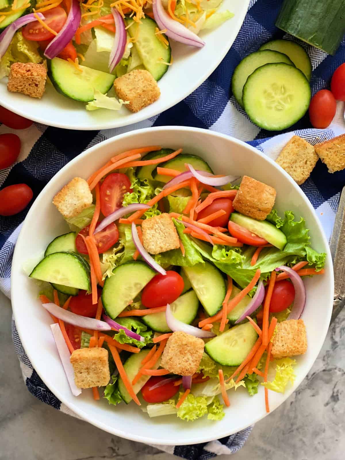 Two white bowls filled with salad with tomatoes, cucumber, shredded carrots, and croutons.