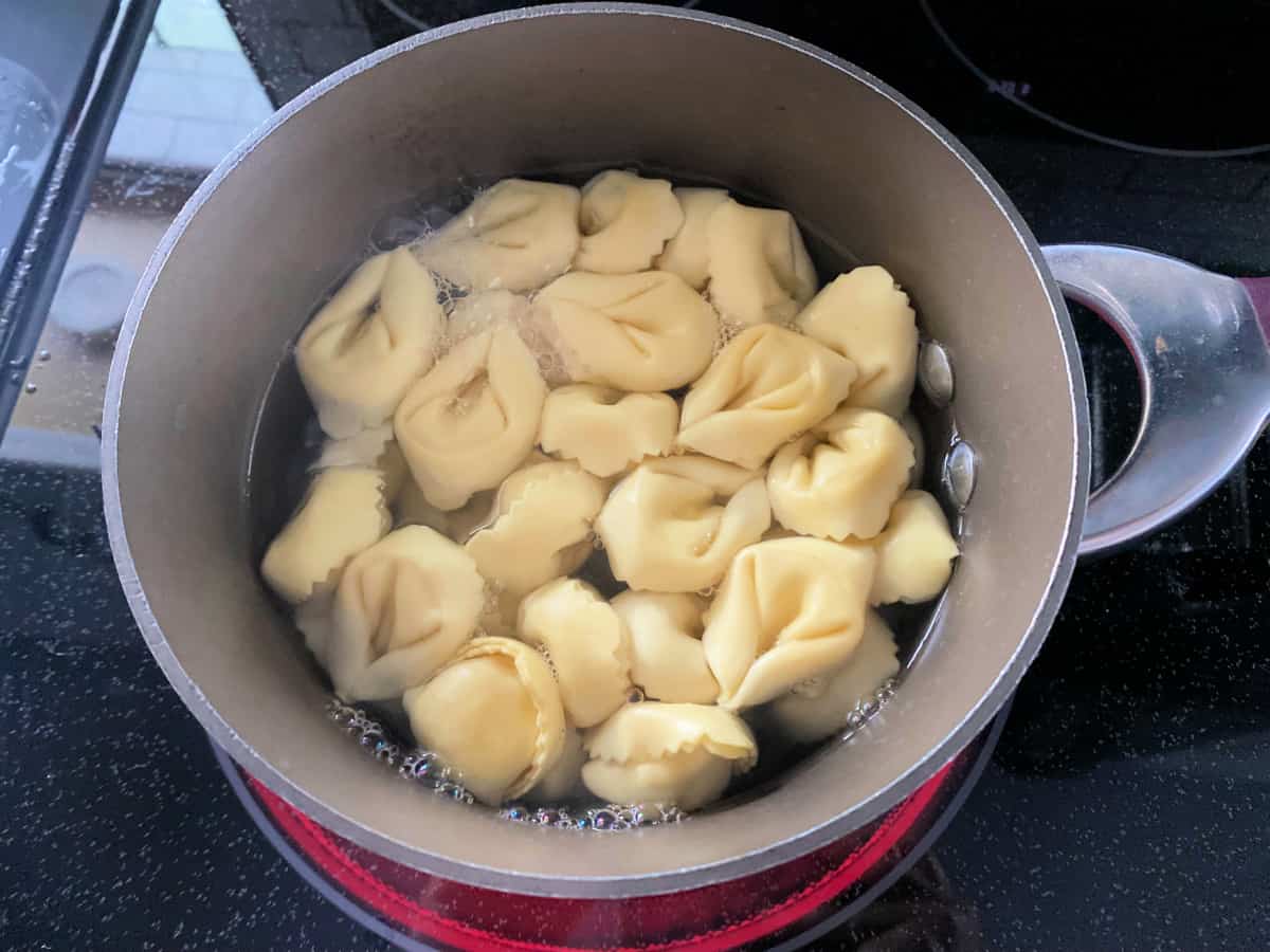 Brown pot on a stove top with tortellini boiling.