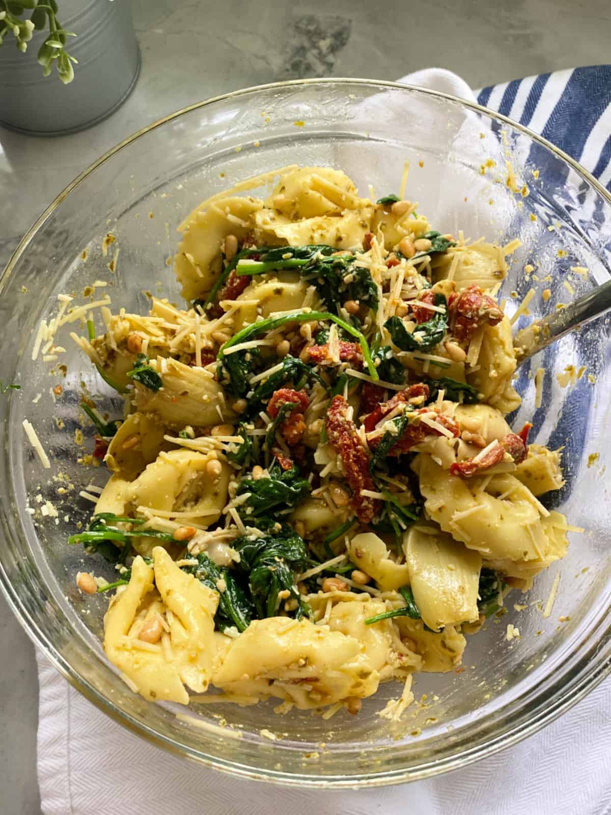 Glass bowl filled with tortellini, spinach, tomatoes, and artichoke hearts.