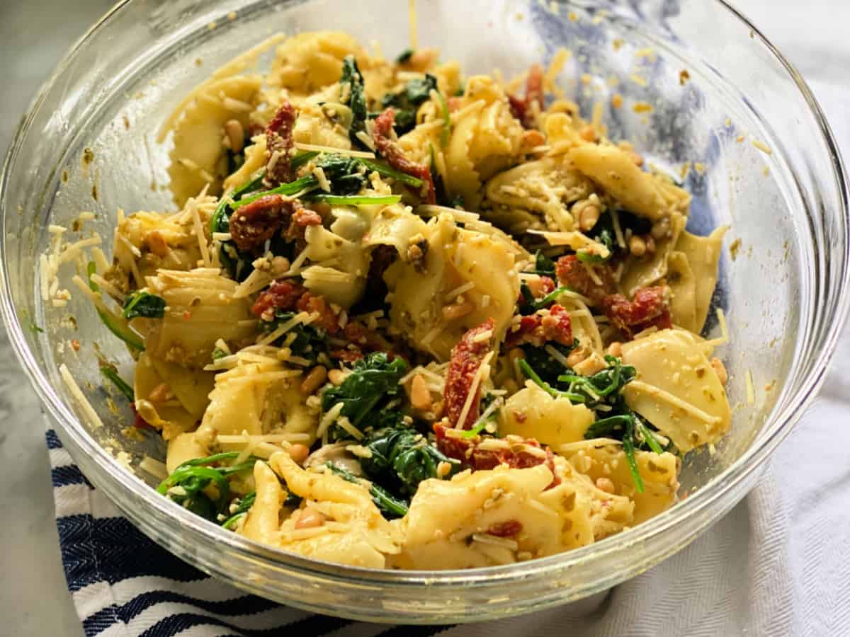 Glass bowl filled with tortellini, tomatoes, spinach, and pesto.