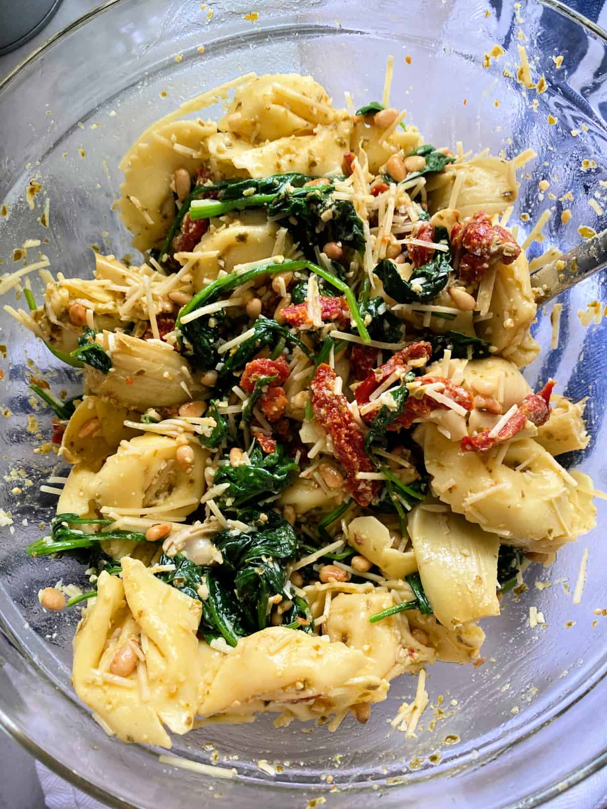 Glass bowl filled with a pesto tortellini salad with sundried tomatoes, and spinach.