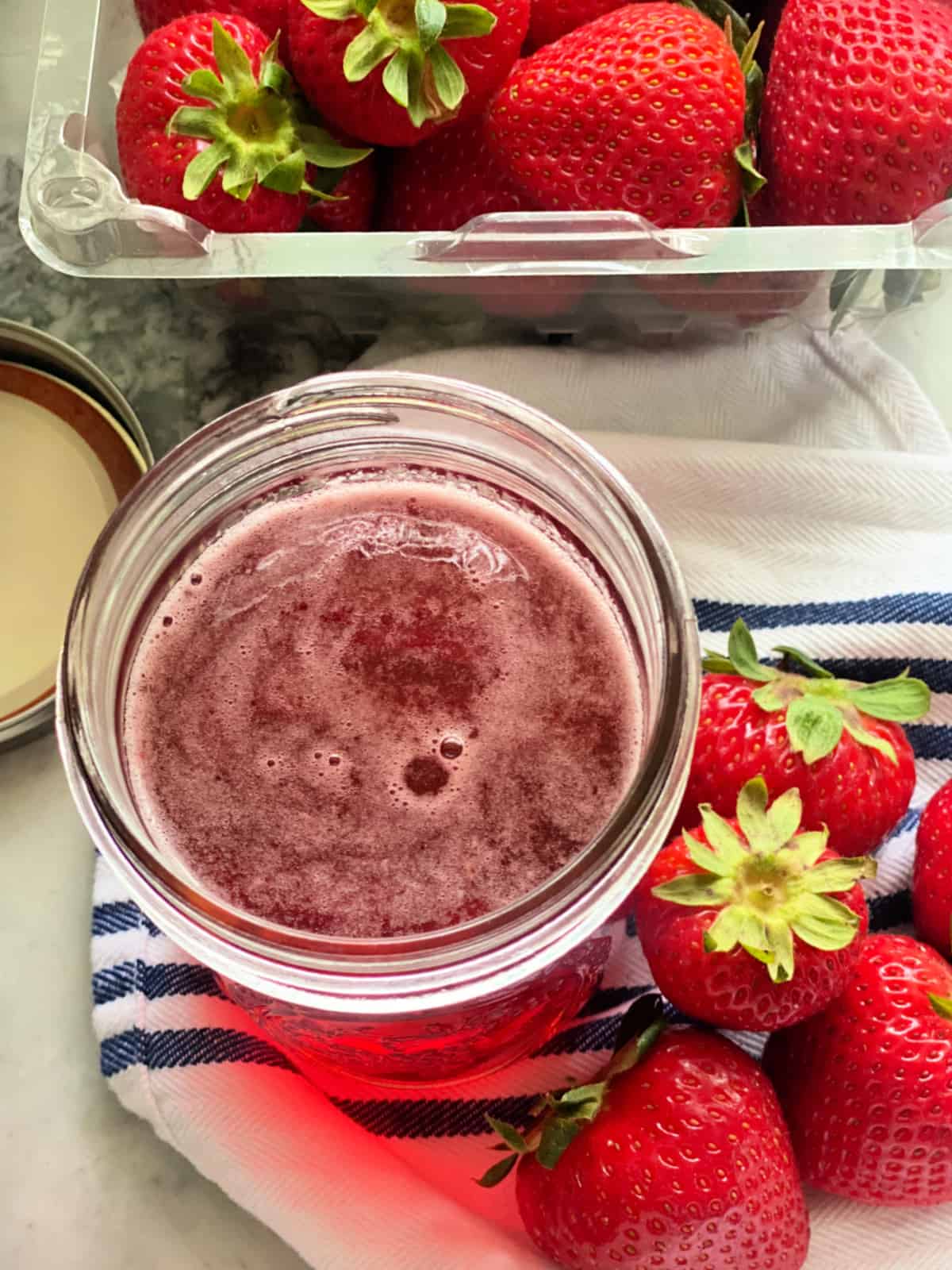 Glass mason jar with pink liquid and fresh strawberries surround the jar.