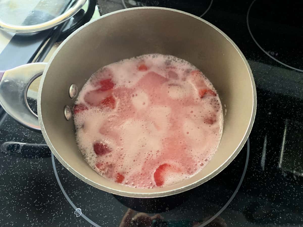 Brown pot with pink bubbling water on a black stove top.