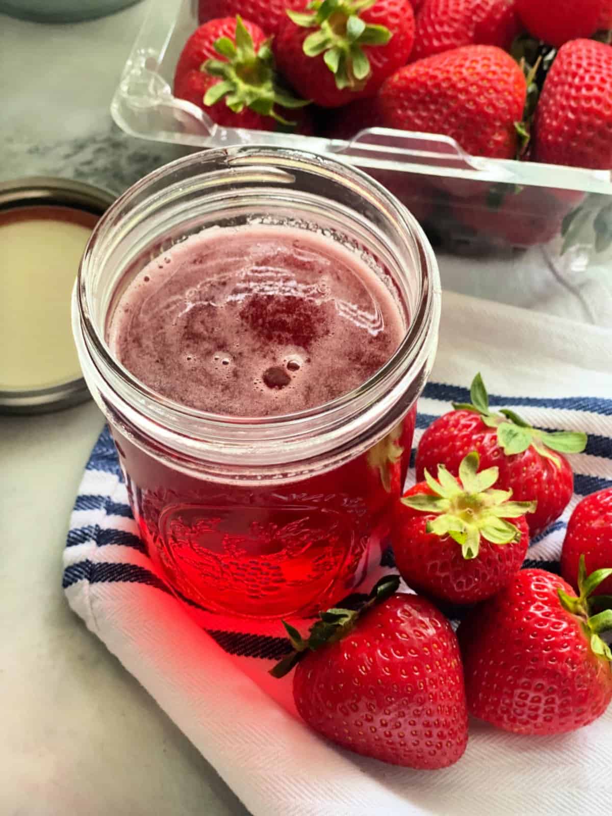 Glass mason jar filled with pink liquid with a basket of strawberries in the background.