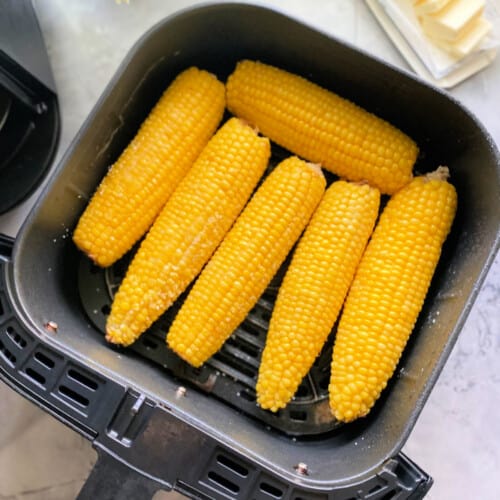 Black Air Fryer basket with 6 corn on the cobs inside the basket.