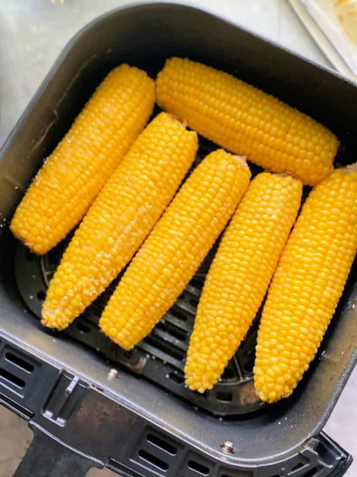 Black Air Fryer basket with 6 corn on the cobs inside the basket.