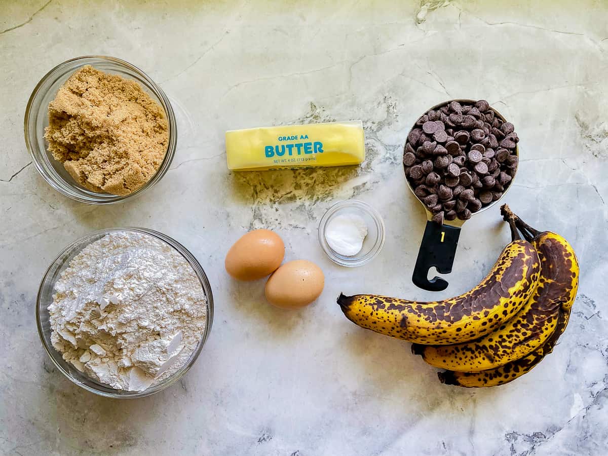 Ingredients on counter; flour, brown sugar, butter, eggs, bananas, baking soda, salt, and chocolate chips.