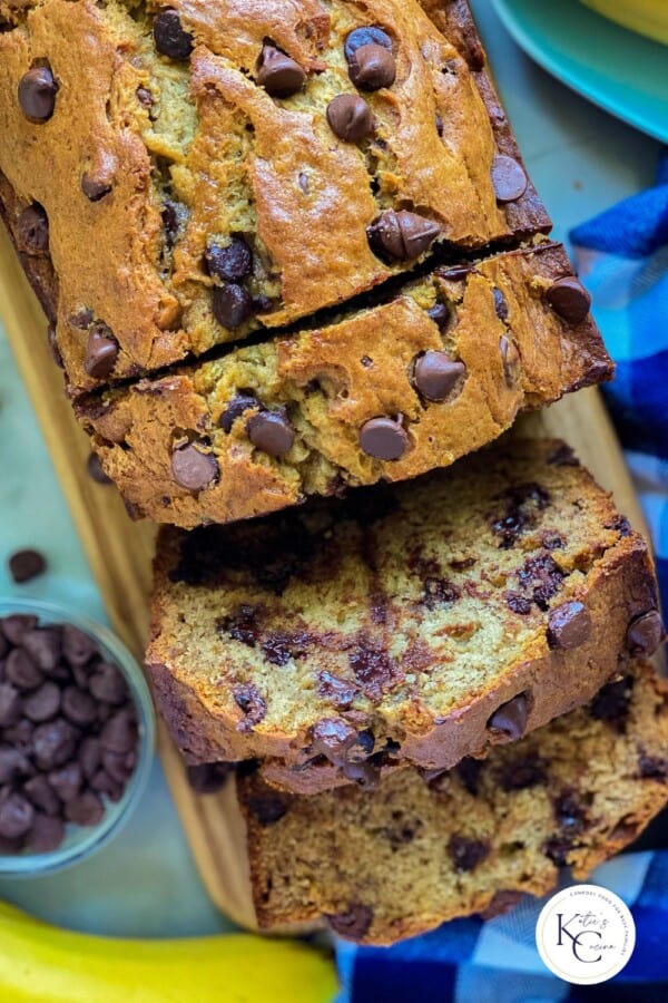 Slices of banana bread on a wood cutting board with logo on right bottom corner.