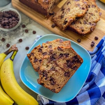 Blue plate with slices of banana bread with chocolate chips with yellow bananas next to the plate.