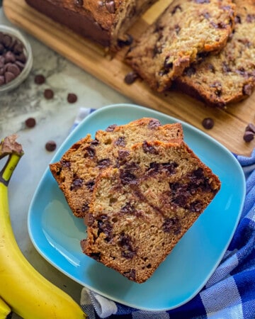 Blue plate with slices of banana bread with chocolate chips with yellow bananas next to the plate.