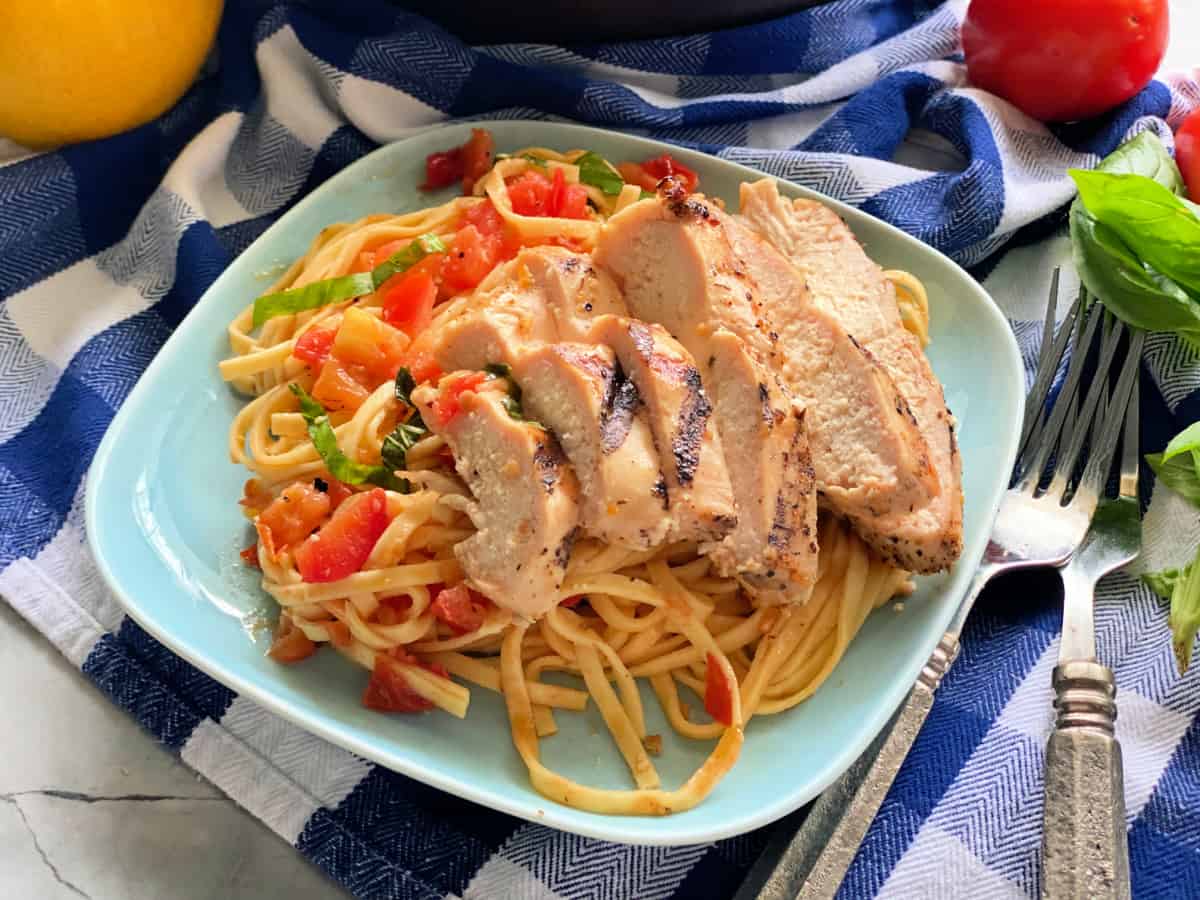 Blue square plate filled with pasta and sliced chicken with two forks next to it.