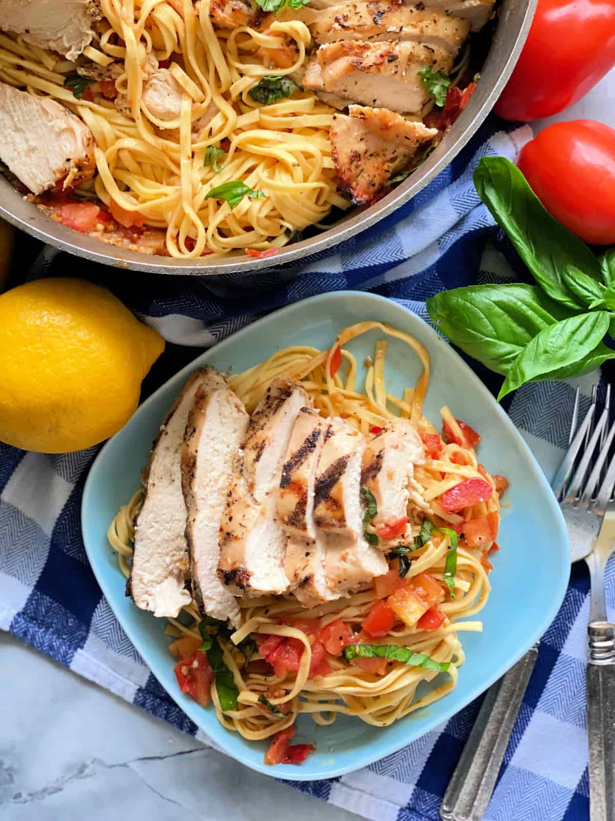 Blue plate filled with pasta and chicken with a skillet filled with the same in the upper left corner.