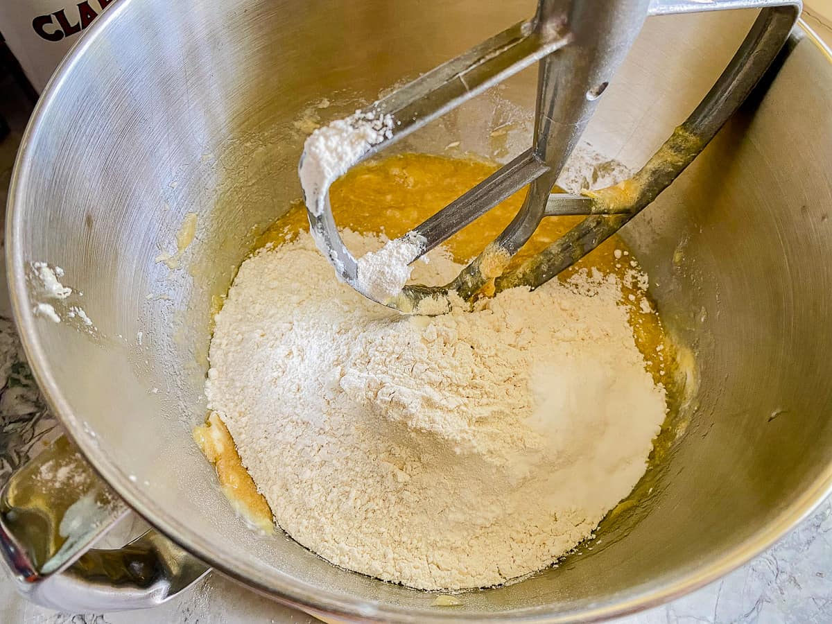 Metal bowl filled with bananas, butter, flour, and flat paddle attachment.