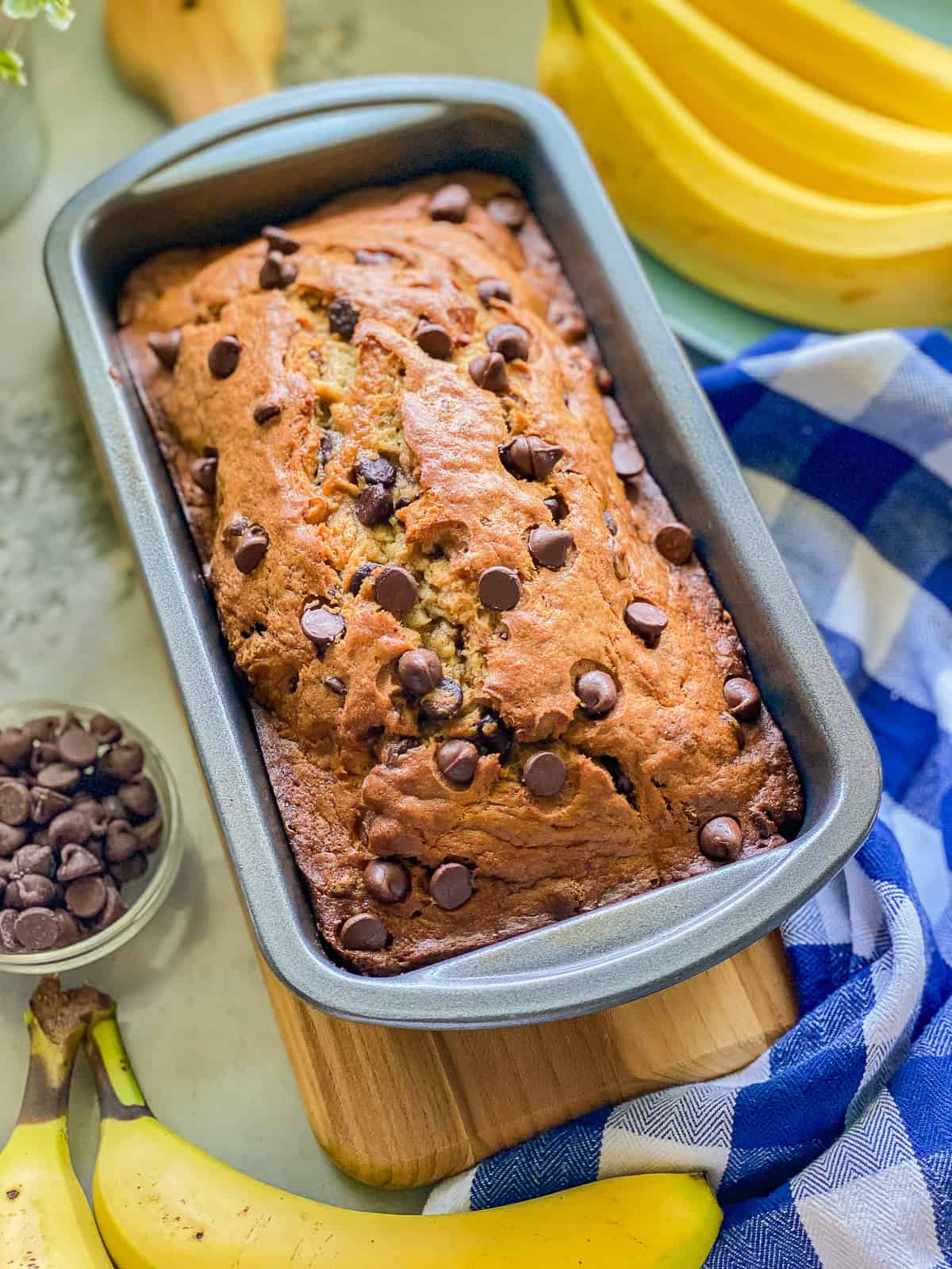 Metal pan filled with baked banana bread with bananas around the pan.