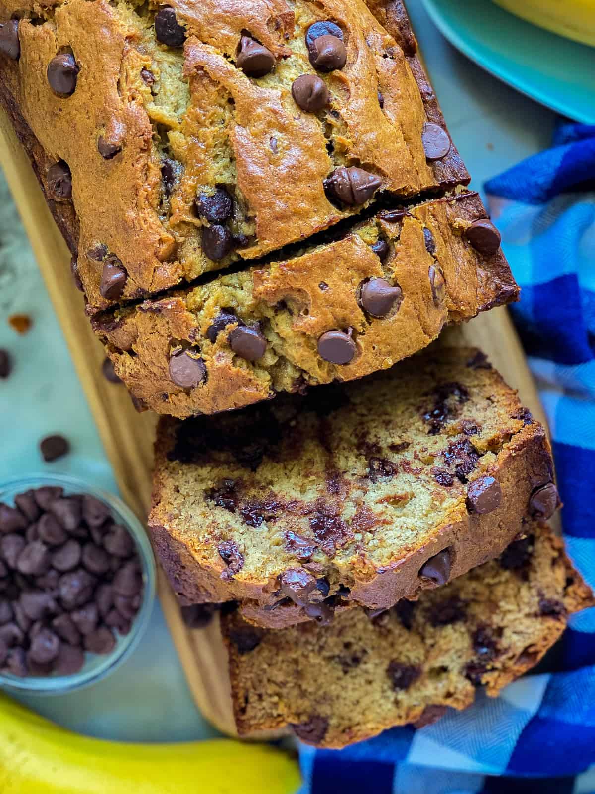 Three slices of banana bread with the loaf attached on a wood cutting board.