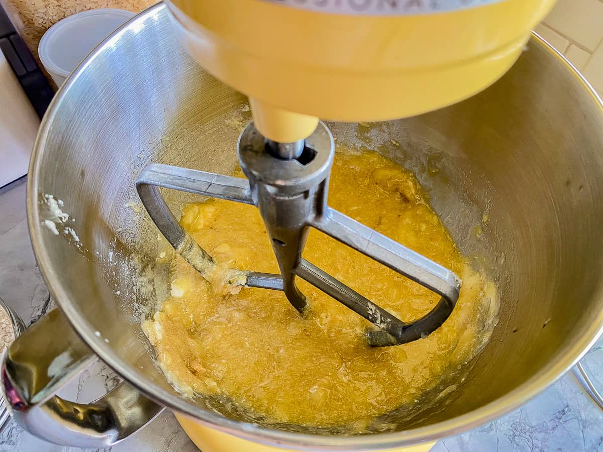 butter and mashed bannanas mixed in a metal bowl fitted with a paddle attachment.