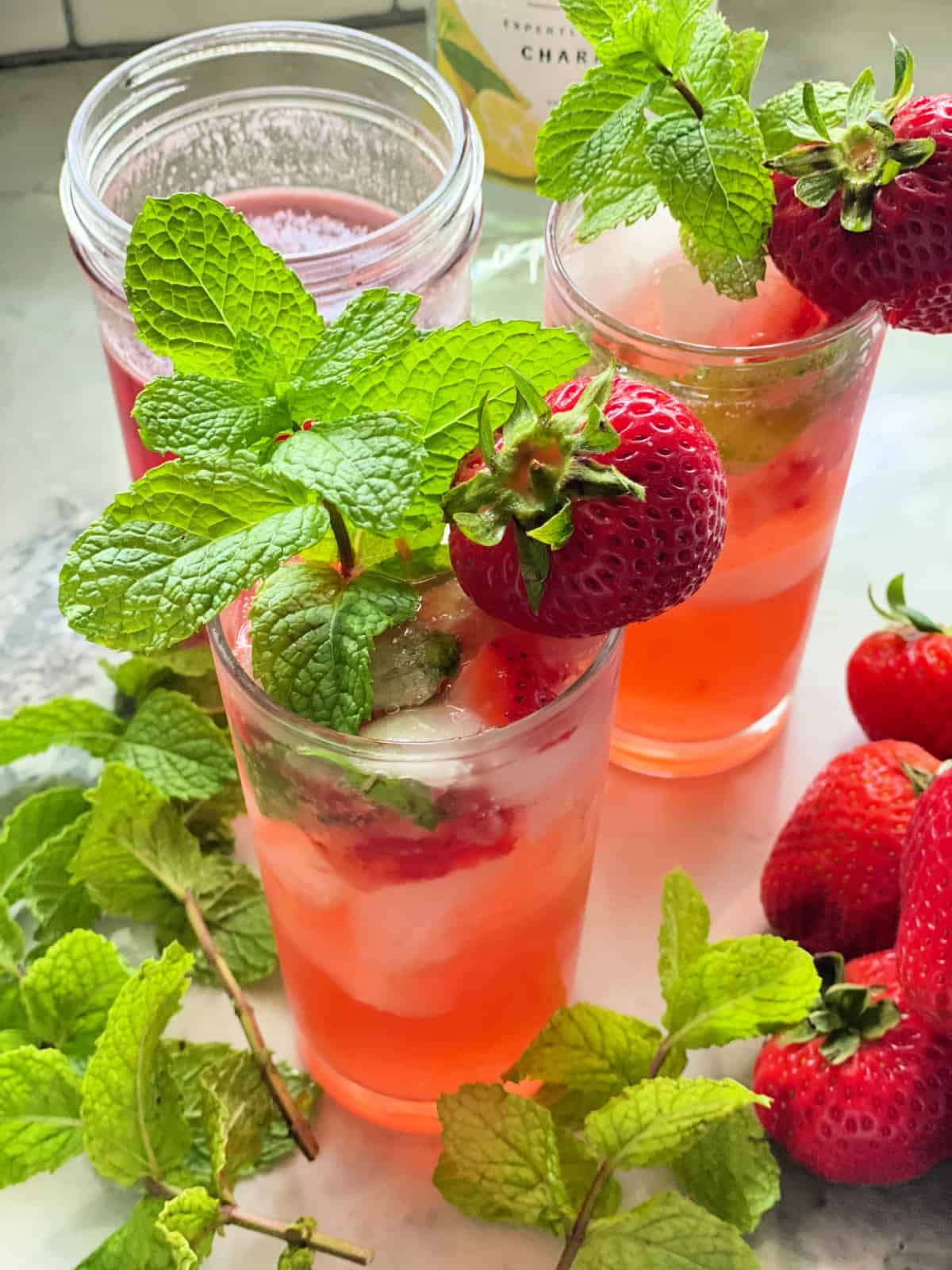 2 glasses filled with mint and strawberry with garnish.