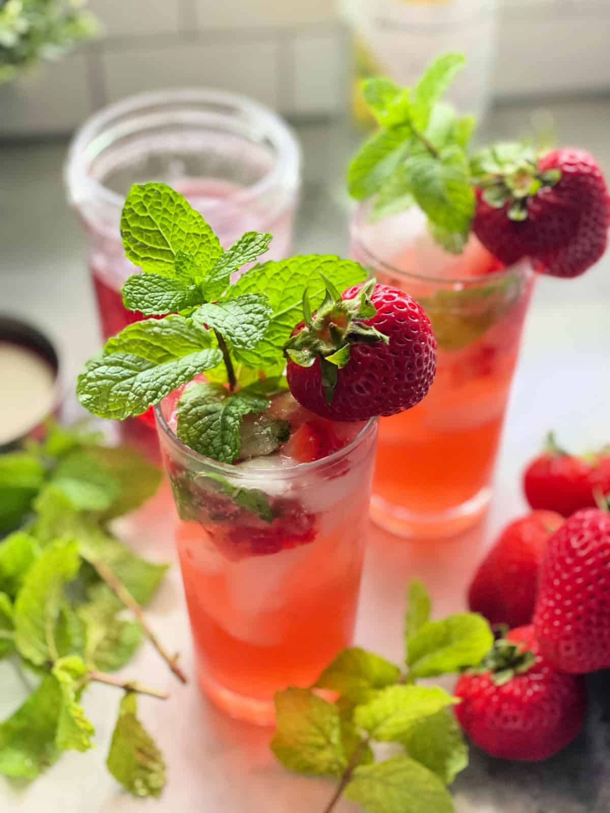 Two glasses with strawberry drink with mint and fresh strawberries for garnish.