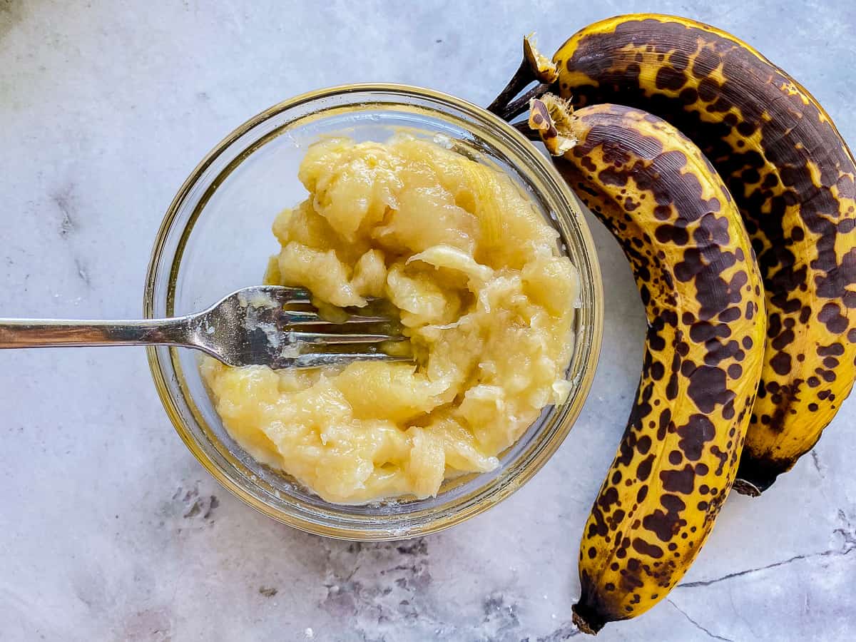 Bowl of mashed bananas with spotted bananas next to the bowl.