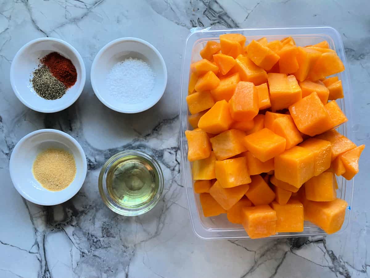 Ingredients on a marble counter: black pepper, paprika, garlic powder, salt, oil, butternut squash.