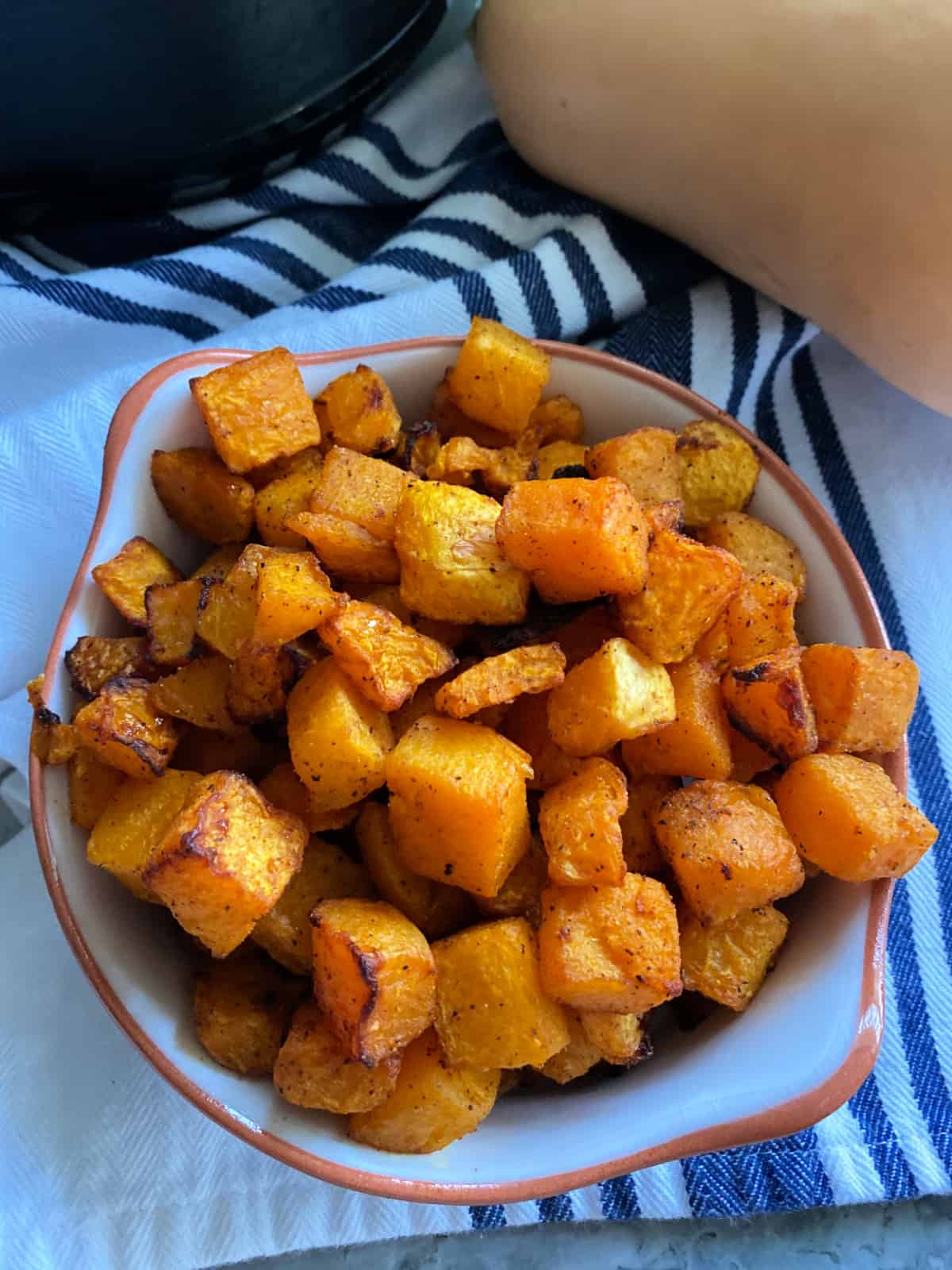 Air fryer butternut squash in a dish on a blue and white striped cloth.