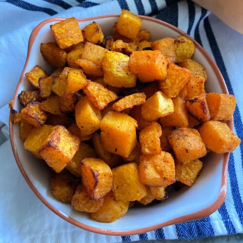 Air fryer butternut squash in a dish on a blue and white striped cloth.
