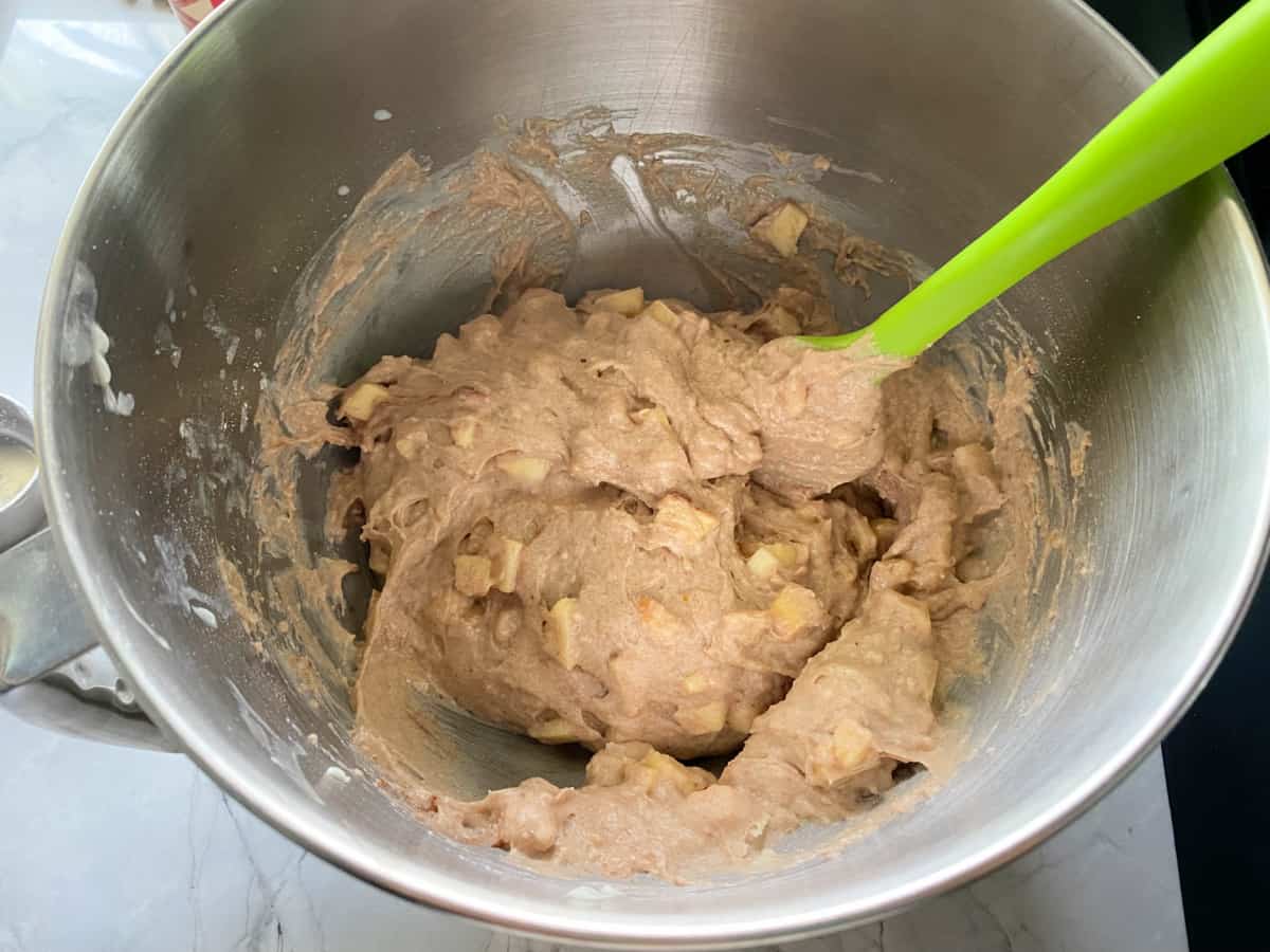 Apple cinnamon muffin mixed batter in a stainless steel bowl with a spatula.