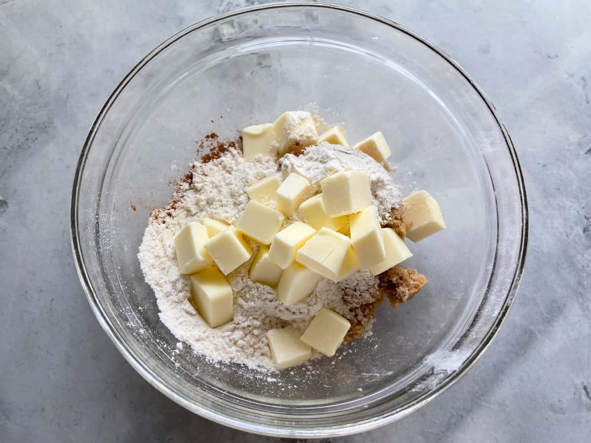 Clear bowl with crumb topping ingredients on a marble counter.