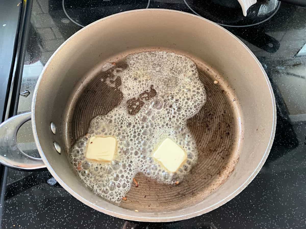Two pads of butter melting in a skillet.