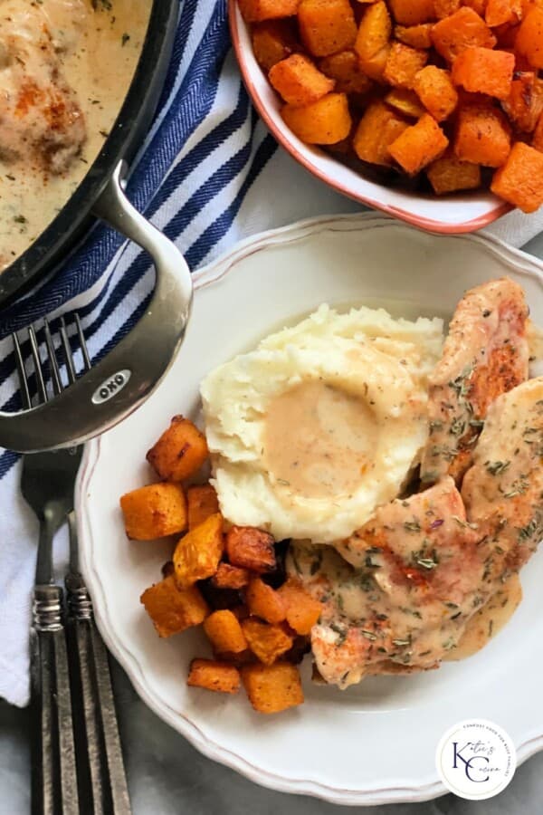 Plate with mashed potatoes, turkey cutlets, and butternut squash and air fryer butternut squash in a dish on a blue and white striped cloth and two forks.