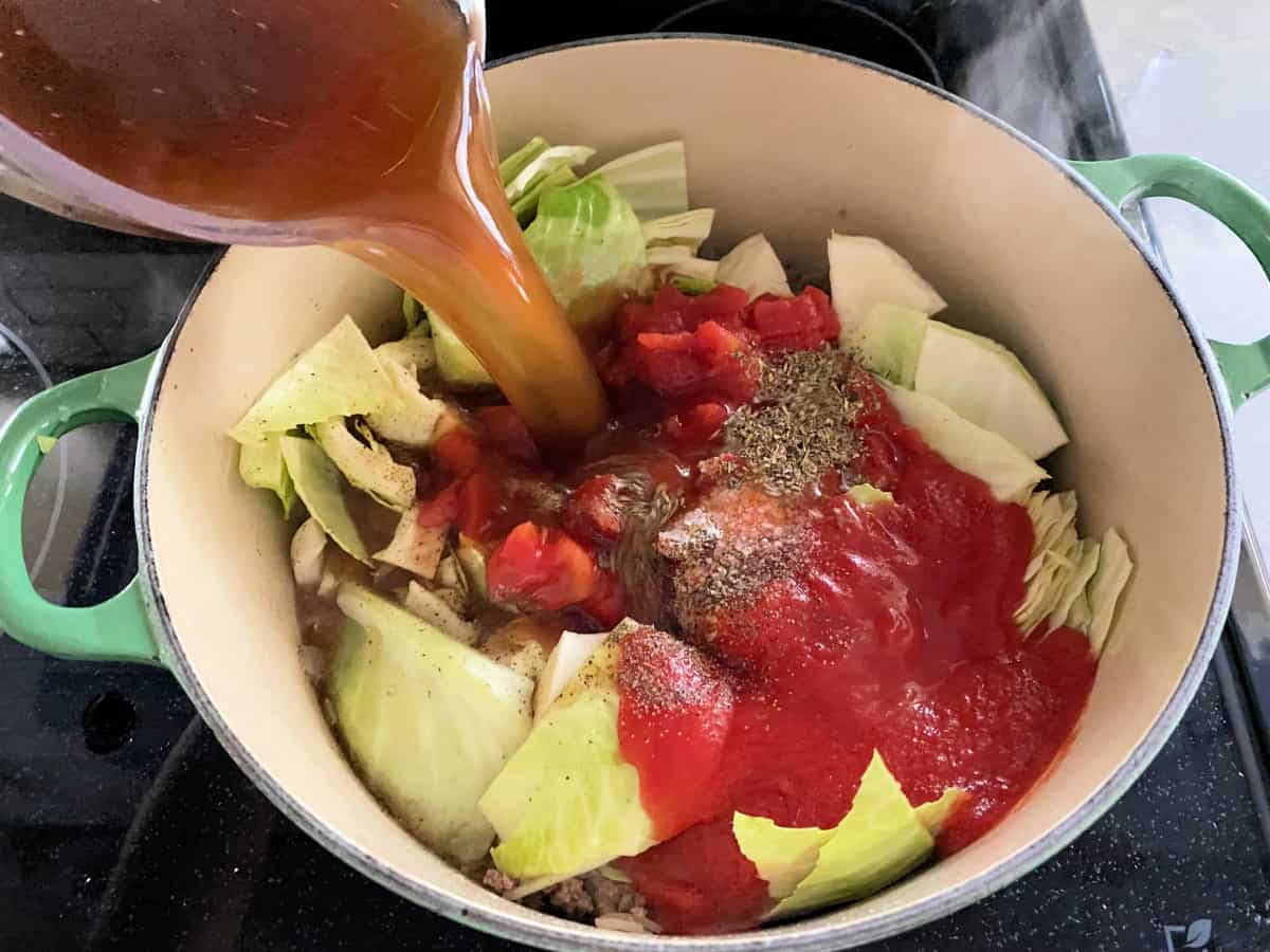 green pot on the stove filled with ingredients for stuffed cabbage soup and broth pouring in.