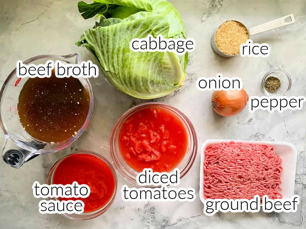 ingredients on the marble counter: beef broth, cabbage, tomato sauce, diced tomatoes, onion, ground beef, rice, pepper