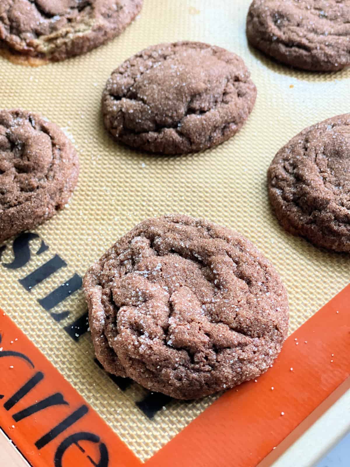 close up of 6 baked chocolate sugar cookies on a cookie sheet.