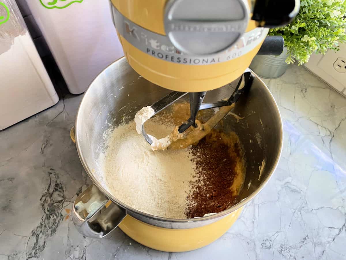 yellow mixer with chocolate sugar cookie dry ingredients on a gray marble counter.