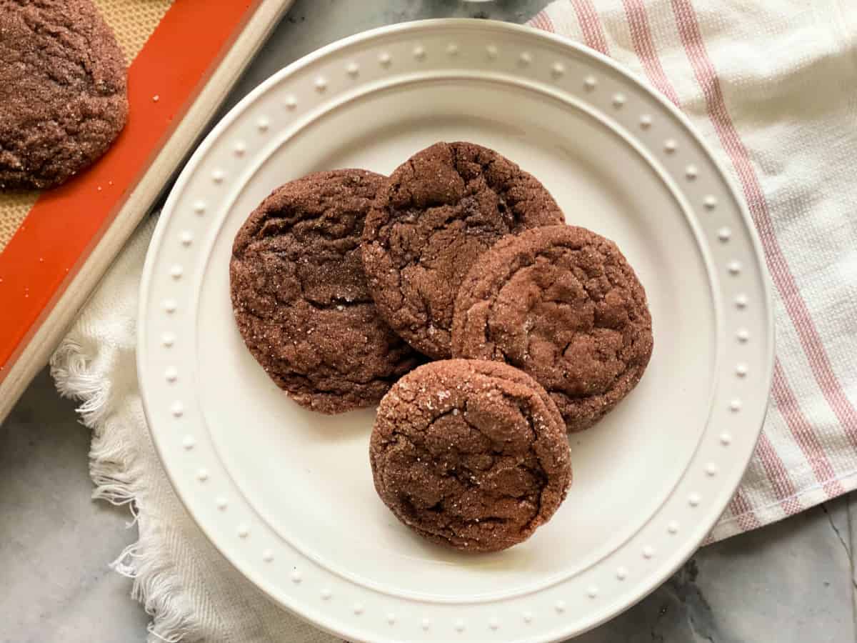 4 chocolate sugar cookies on a white plate with a pink striped white cloth in the background.