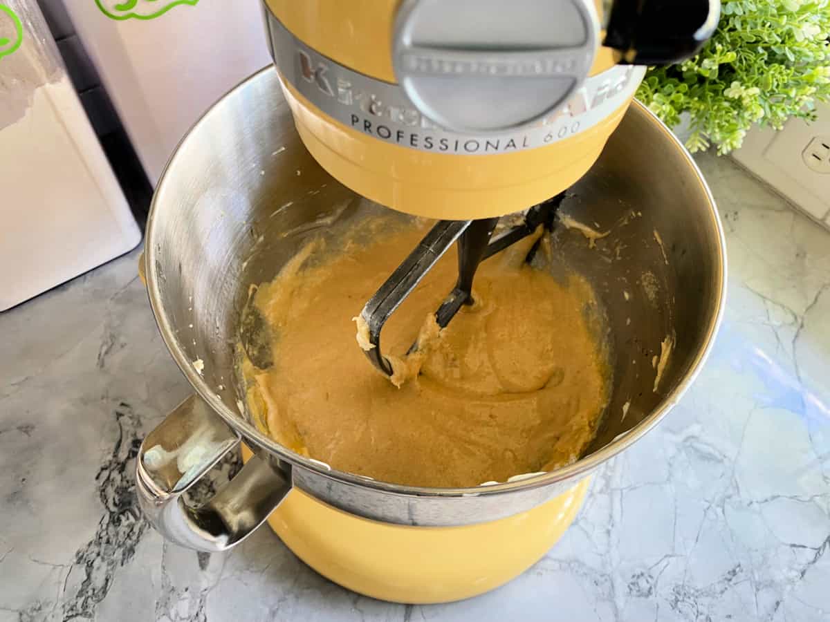 yellow mixer with creamed butter and sugar on a gray marble counter.