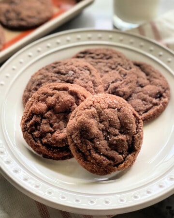 4 chocolate sugar cookies on a white plate with a pink striped white cloth in the background.