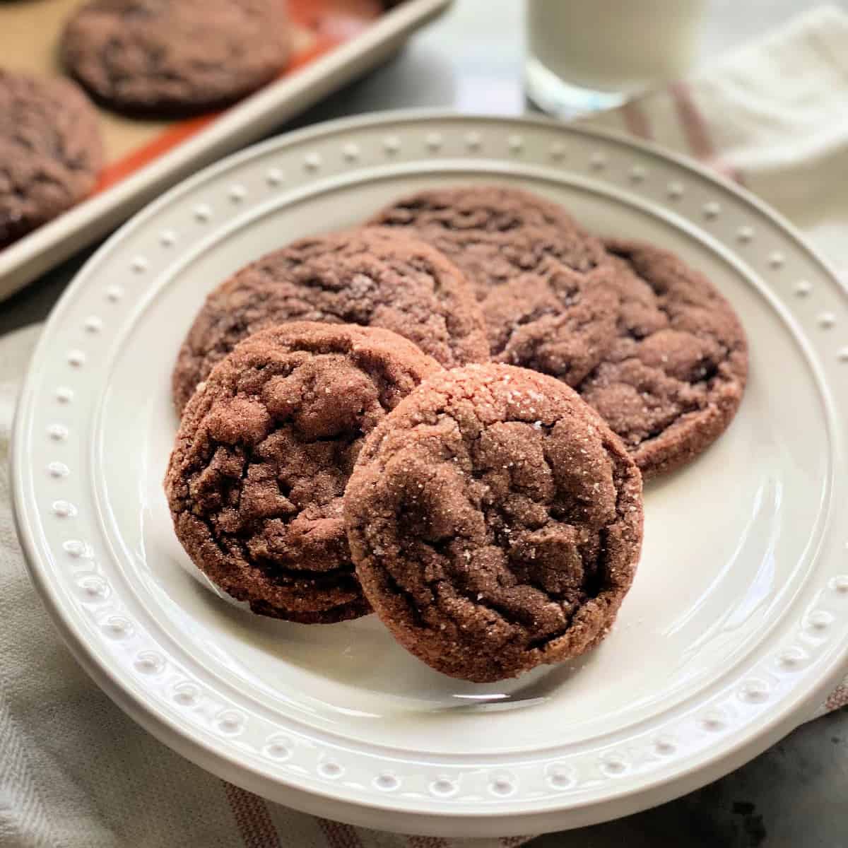 4 chocolate sugar cookies on a white plate with a pink striped white cloth in the background.