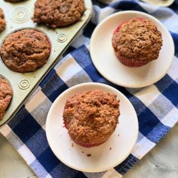 2 apple cinnamon muffins on a small white plates on a blue and white checkered cloth, and 5 muffins.