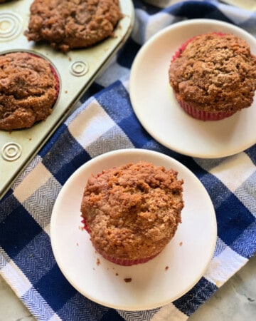 2 apple cinnamon muffins on a small white plates on a blue and white checkered cloth, and 5 muffins.