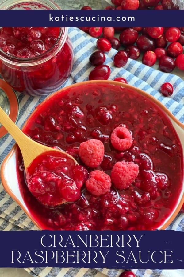 Text on image: "cranberry raspberry sauce" with photo of wooden spoon with cranberry raspberry sauce in a bowl on a blue and white stripped cloth with a jar of sauce and cranberries scattered in the background.