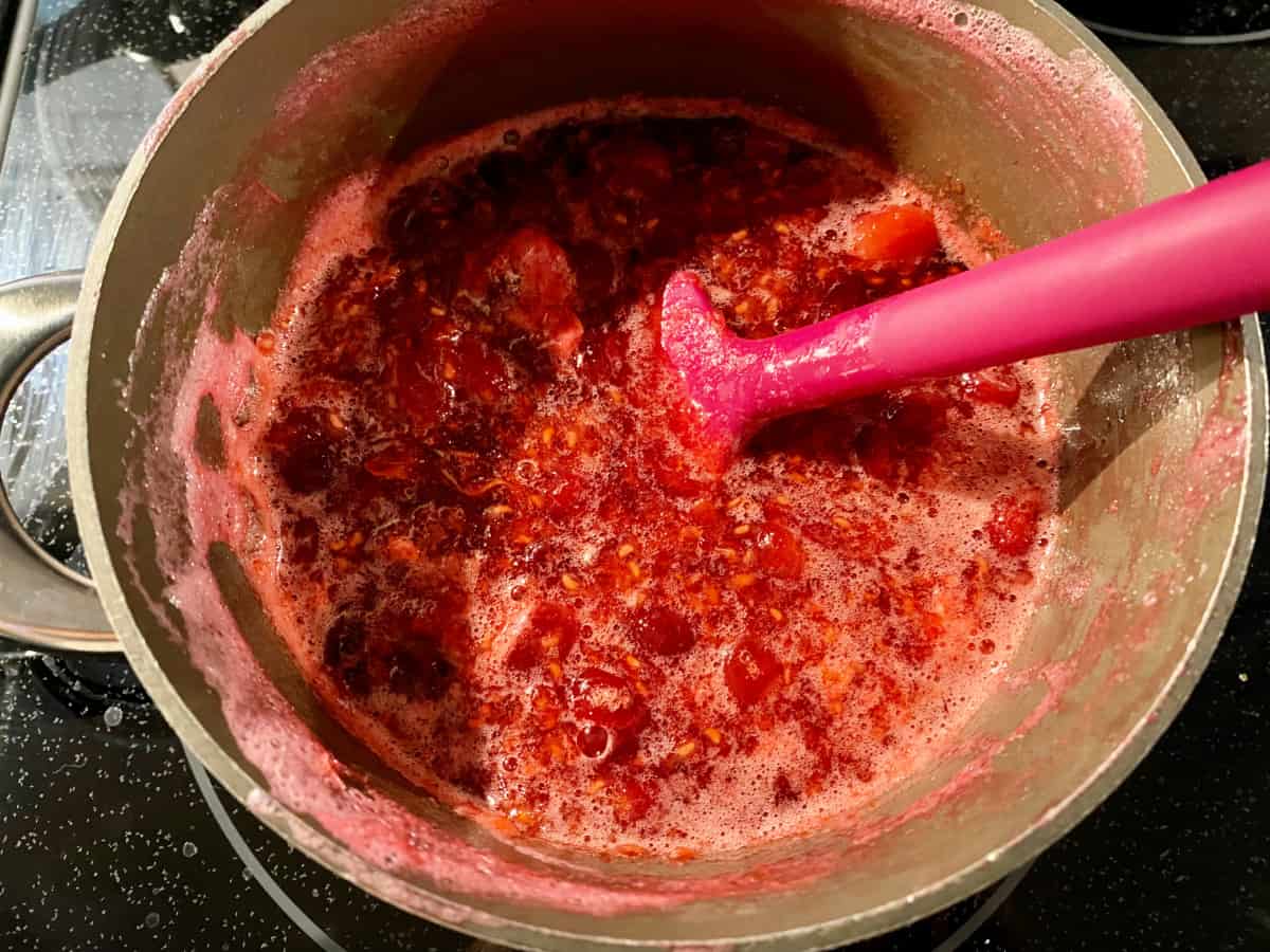 Cranberry raspberry sauce mixed in a pot on the stove with a spatula.