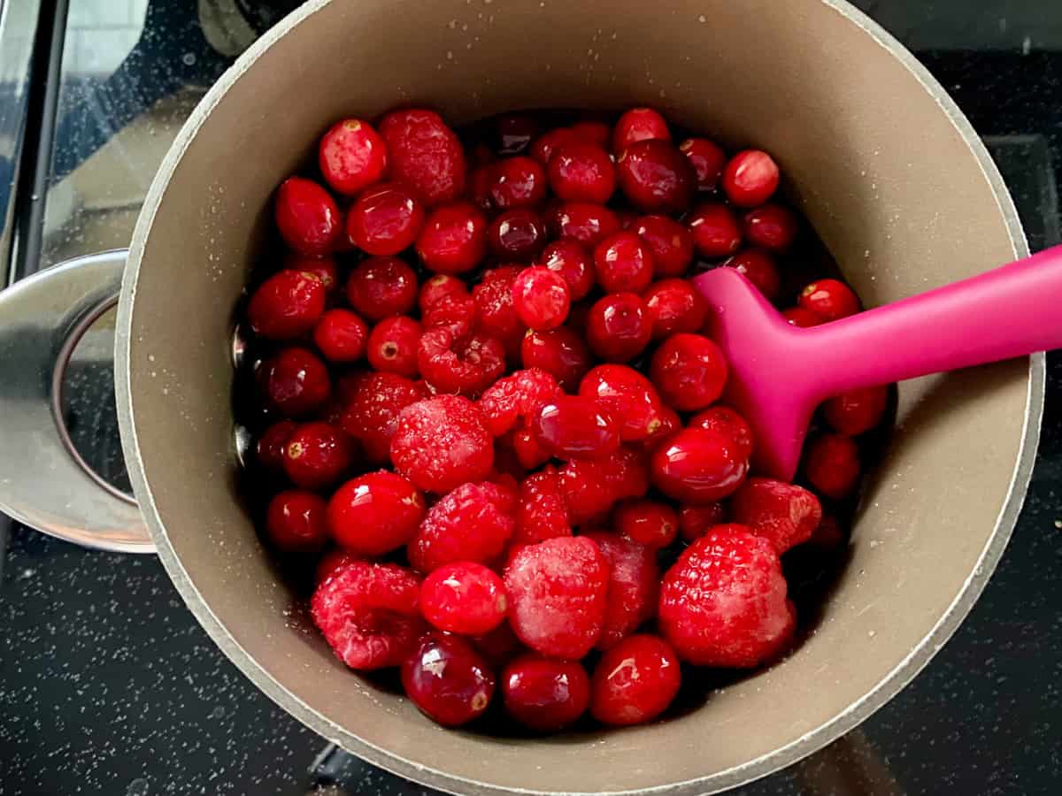 cranberries and raspberries in a pot with a spatula.