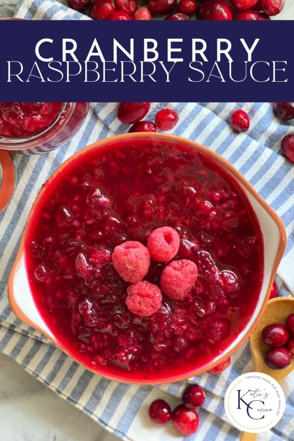 Text on image: "Cranberry raspberry sauce" with photo of cranberry raspberry sauce in a bowl on a blue and white stripped cloth with a jar of sauce, wooden spoon, and cranberries scattered in the background.