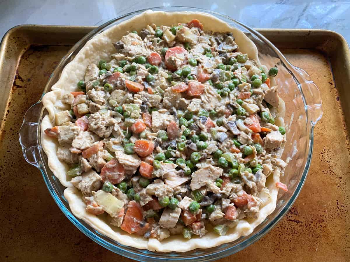 Glass pie plate with chicken, carrots, and peas on top of pie crust.