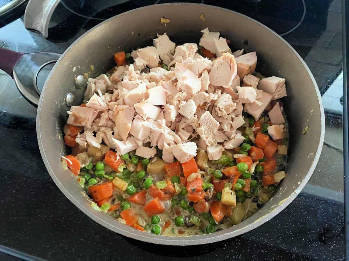 Brown skillet filled with diced chicken, carrots, peas, potatoes, and mushrooms.