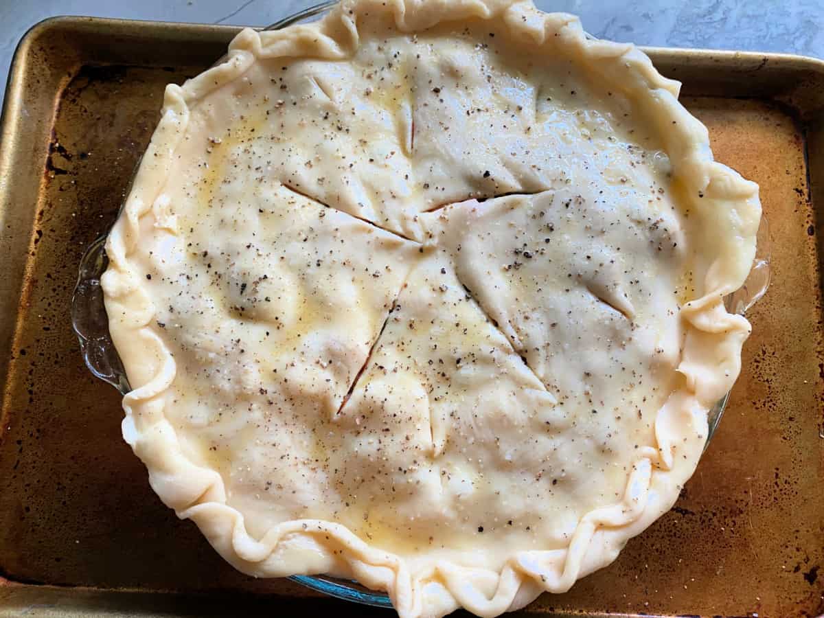 Raw pie dough over a pie plate with five long slits in the middle and salt and pepper on top.