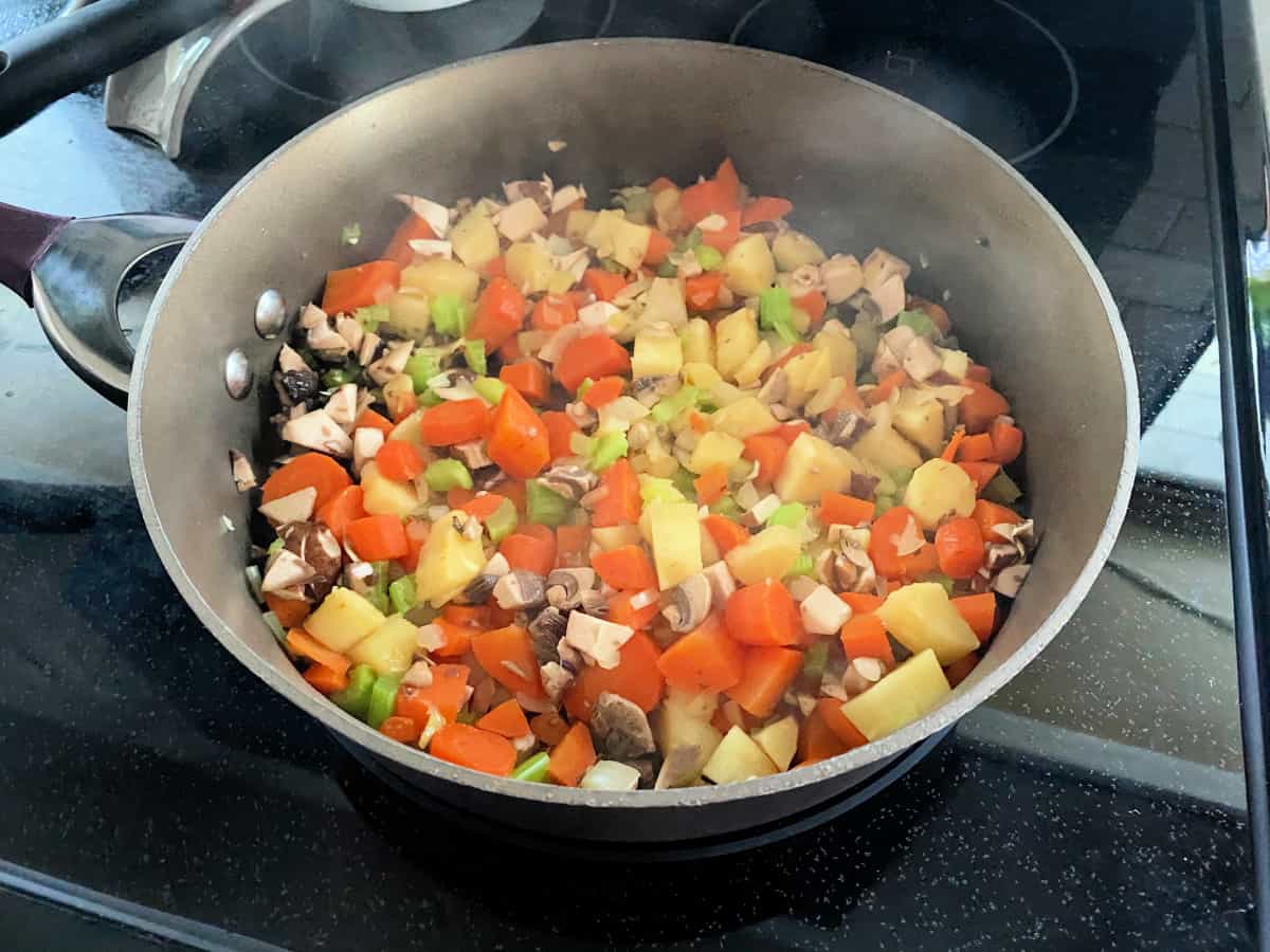 Brown skillet filled with potatoes, carrots, peas, and mushrooms.