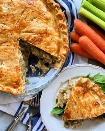 Pie with a slice taken out and a piece of savory pie resting on spinach on a white plate.